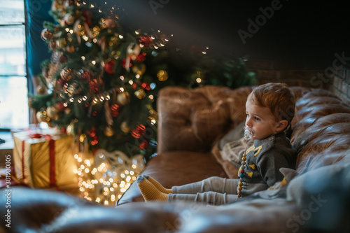 Portrait of a baby on the sofa near the Christmas tree with gifts.