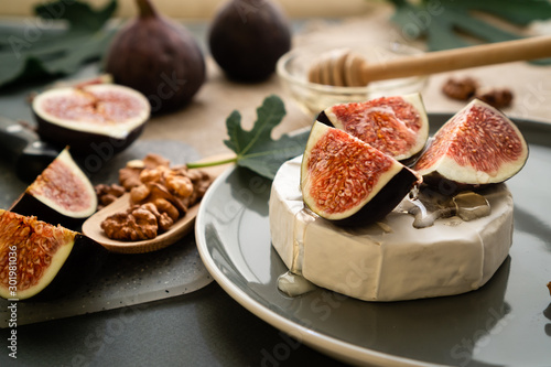 Details of gourmet food on a plate of camembert cheese and figs. Fruit sliced with honey and nuts.