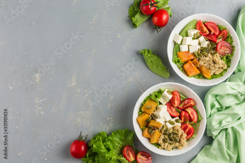 Salad bowl of quinoa, cherry tomato, baked pumpkin, pumpkin seeds, feta cheese and fresh lettuce.