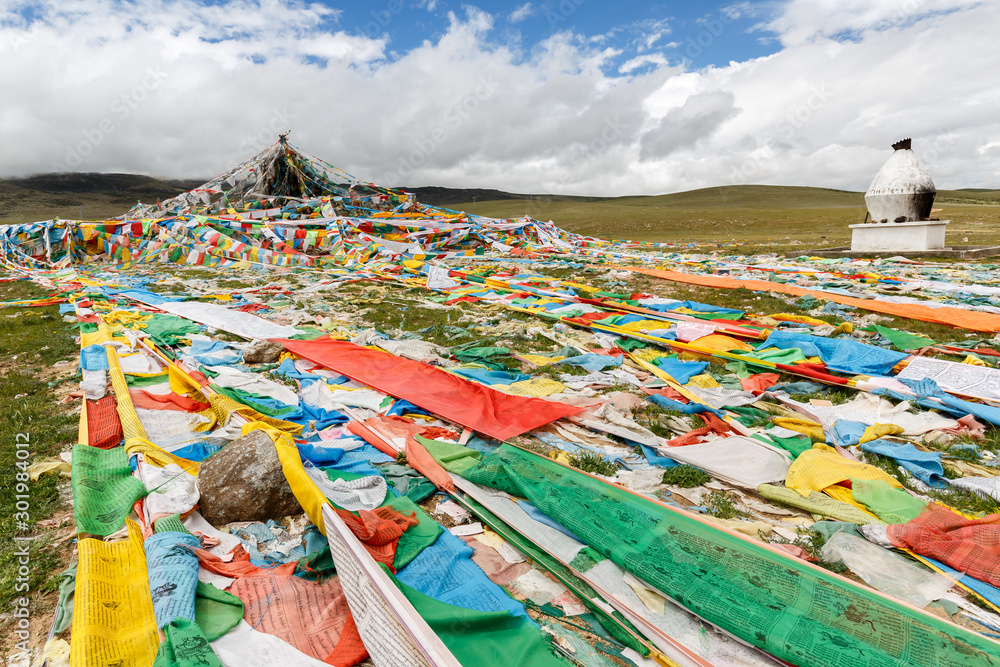 TIBETAN PLATEAU, TIBET / CHINA - Aug 1, 2017: Prayer flags lying on the ground in the grasslands of the tibetan plateau. They promote compassion, peace, strength, wisdom. On right a traditional oven.