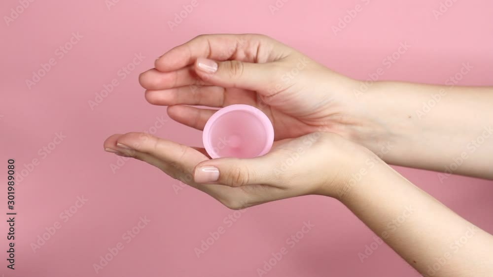 Close up of a young woman hands holding reusable pink silicone menstrual cup on pink background. Zero waste menstruation hygiene concept.