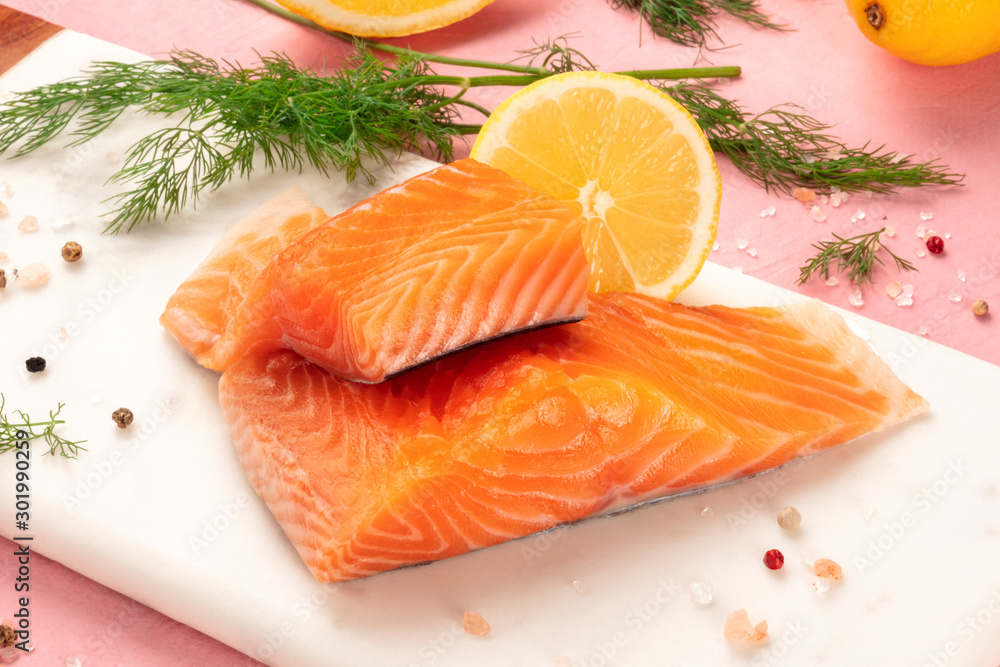 Slices of salmon with lemon and dill, close-up with salt and pepper, cooking fish, on a pink background Slices of salmon with lemon and dill, close-up with salt and pepper, cooking fish, on a pink background