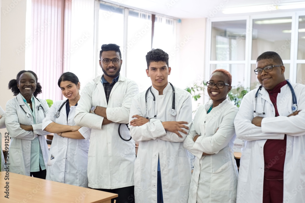 a group of doctors in the hospital corridor. Team of mixed race young men in white coats, with phonendoscopes, smiling a group of doctors in the hospital corridor. Team of mixed race young men in white coats, with phonendoscopes, smiling