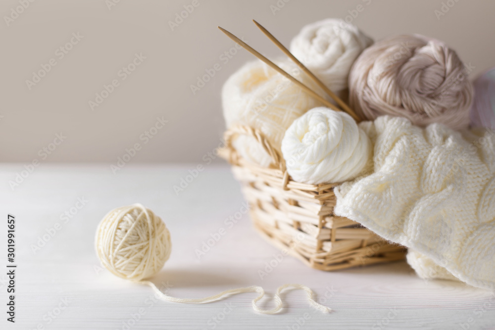 White and beige yarn for knitting in a basket. Knitting needles.