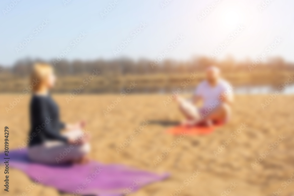 A man practices yoga with a woman on the riverbank. Golden sand, background, blurred A man practices yoga with a woman on the riverbank. Golden sand, background, blurred