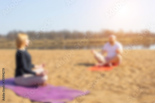 A man practices yoga with a woman on the riverbank. Golden sand, background, blurred