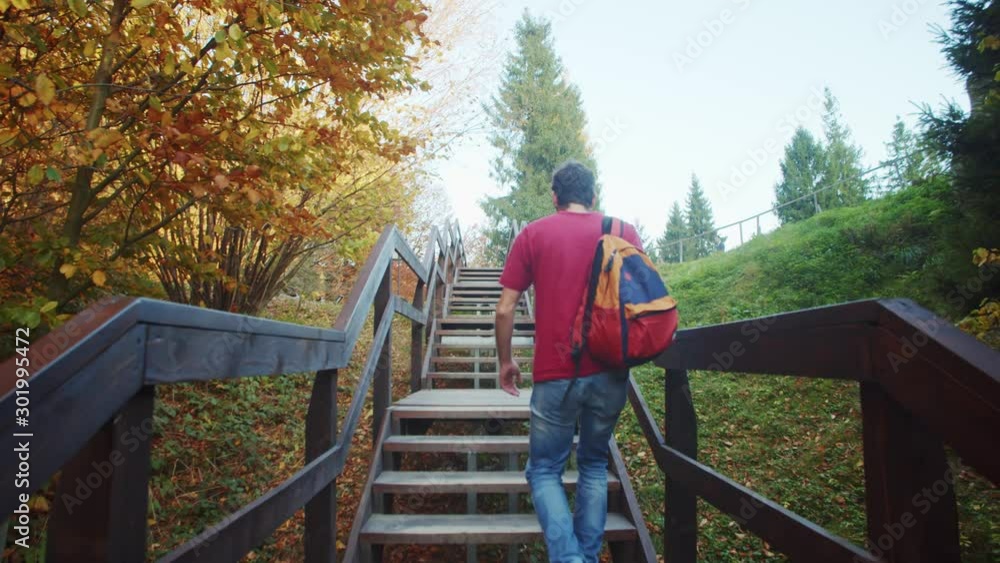 Tousit backpacker climping upstairs in beautiful park at autumn season. Back of young excited man ascenting high mountain forest on wooden stairs walkway. Tousit backpacker climping upstairs in beautiful park at autumn season. Back of young excited man ascenting high mountain forest on wooden stairs walkway.