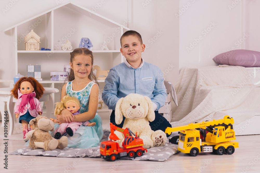 beautiful happy caucasian children sitting in their room, boy with car, girl  with doll - obrazy, fototapety, plakaty 
