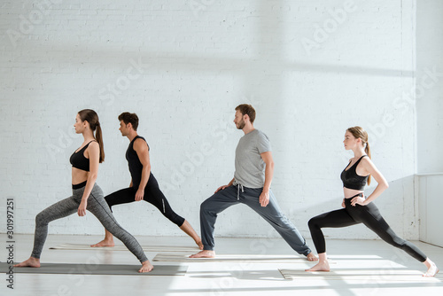 side view of young people in sportswear practicing yoga in warrior I pose