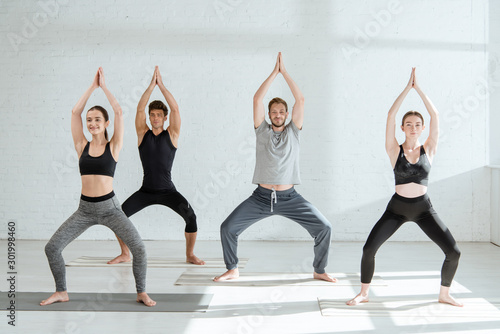 young people in sportswear practicing yoga in goddess pose with raised prayer hands