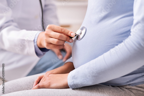 Unrecognizable Doctor Holding Stethoscope Near Pregnant Woman's Belly Indoor, Cropped