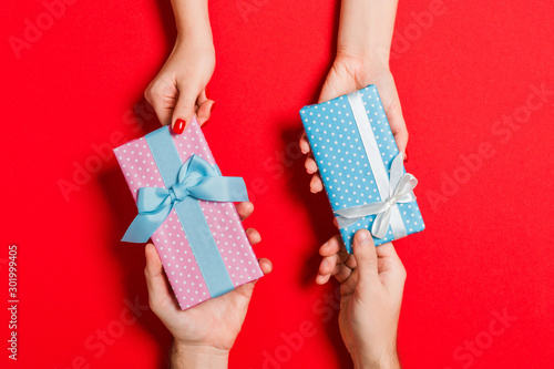 Top view of a woman and a man exchanging gifts on colorful background. Couple give presents to each other. Close up of making surprise for holiday concept © sosiukin