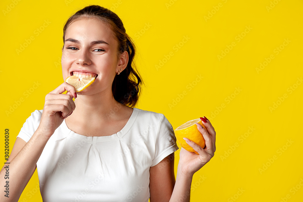 Ταπετσαρία A girl in a white T-shirt is eating a lemon, on a bright yellow background