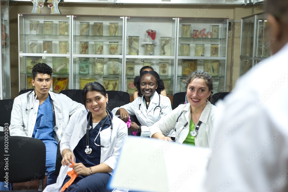 medical teacher, conducts a lesson for medical students. A group of young people of different gender, mixed races, sit on chairs in the classroom