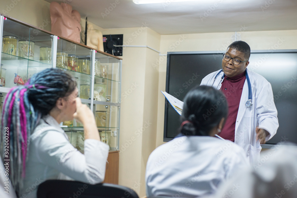 medical teacher, conducts a lesson for medical students. A group of young people of different gender, mixed races, sit on chairs in the classroom medical teacher, conducts a lesson for medical students. A group of young people of different gender, mixed races, sit on chairs in the classroom