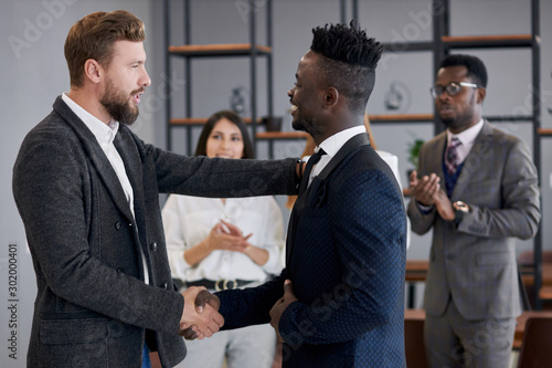 multi-ethnic team after successful meeting shake hands to each other. African and caucasian executives in tuxedo in office photo