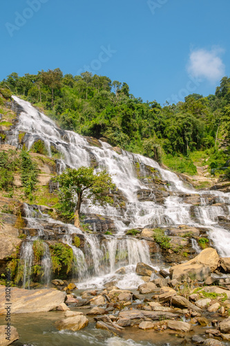 scenery view of waterfall in the lush green forest during day time with strong sunlight