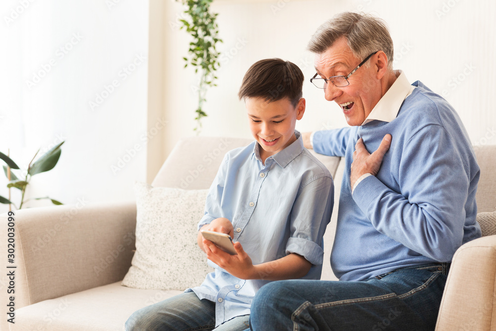 Grandson Teaching Grandpa Use Phone Sitting On Sofa At Home Grandson Teaching Grandpa Use Phone Sitting On Sofa At Home