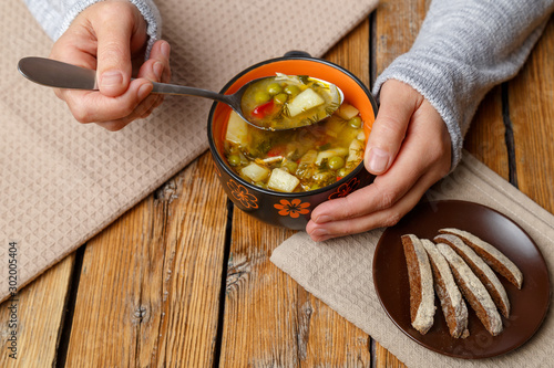 Female hands hold a plate with vegetable soup with chicken. Plate with soup and croutons on a wooden background. Healthy eating concept.