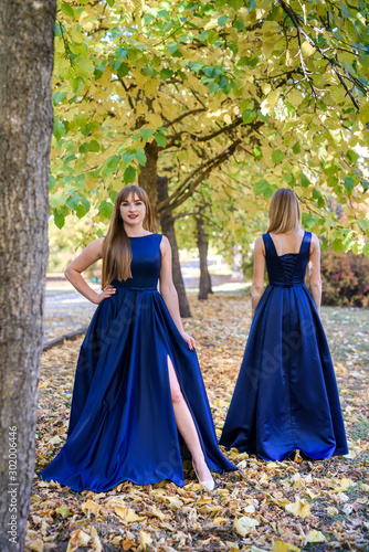Two very beautiful young ladies in fashionable blue dresses in autumn park.
