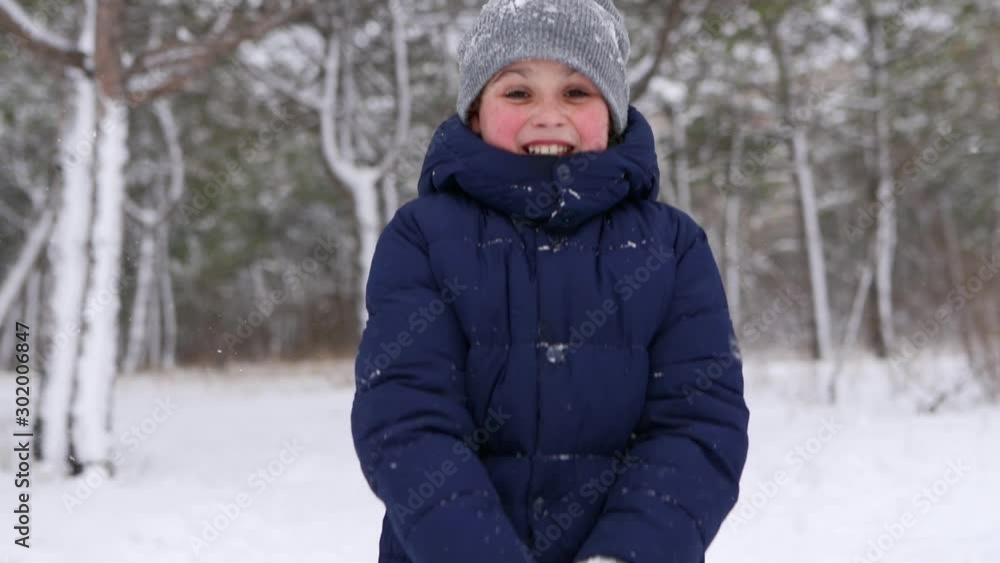 Happy boy in navy jacket play with snow and throw it up to the air in the woods on frosty winter day. Cheerful child in stylish winter outfit enjoy first snowy weather in forest park. Slow motion. Happy boy in navy jacket play with snow and throw it up to the air in the woods on frosty winter day. Cheerful child in stylish winter outfit enjoy first snowy weather in forest park. Slow motion.