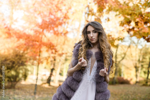 Woman in fashion beige dress and fur coat posing in autumn landscape. Trend clothes
