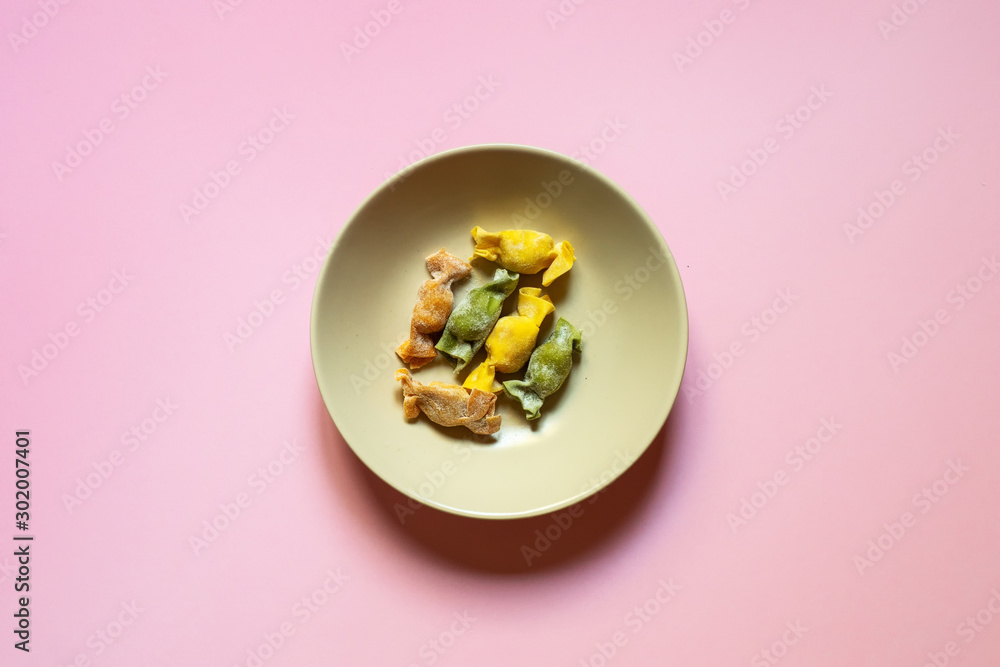 Stuffed Pasta with caramelle shape served in a cream bowl over a coral pink background top view