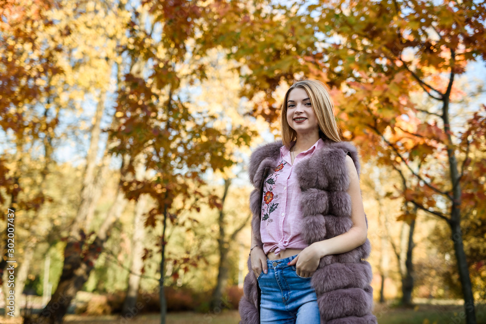 Fashion woman. Smiling girl in fur coat posin in autumn park with trees and ivy Fashion woman. Smiling girl in fur coat posin in autumn park with trees and ivy