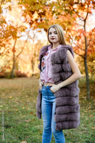 Fashion woman. Smiling girl in fur coat posin in autumn park with trees and ivy © RomanR