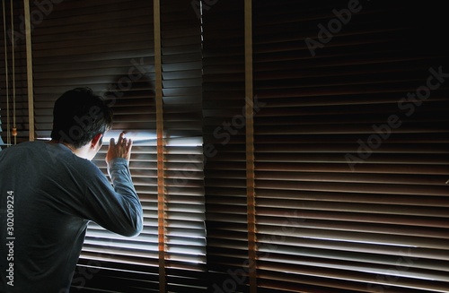 Man looking through wooden blinds from a dark room
