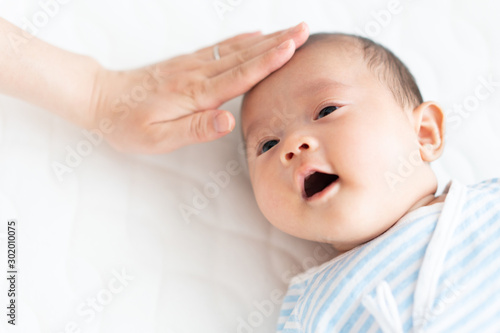 赤ちゃんの額に手を当てて熱を計る女性