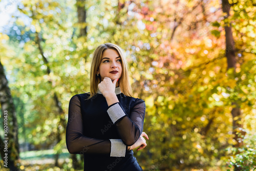 Female porteait in autumn park. Beaurtiful woman in black dress posing with yellow trees Female porteait in autumn park. Beaurtiful woman in black dress posing with yellow trees