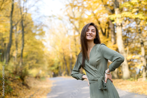 Portrait of brunette woman in green dress posing in autumn park