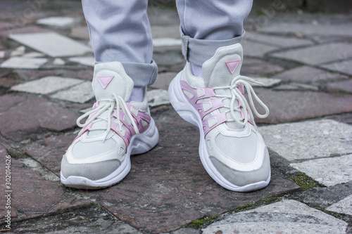 beautiful white sneakers with gray and pink closeup on a female leg in gray jeans on a background of street tile