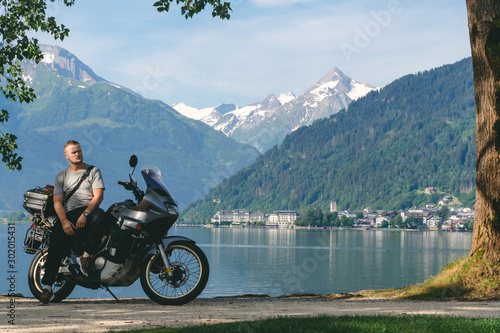 Biker standing with traveler motorcycle. Copy scpace, Vacation and hobby concept, adventure on two wheels. Sunny summer day in the Alpine mountains. Zell am see lake on background Austria. photo