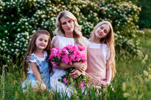 А family of mother and two qute daughters with peonies. Concept of happy motherhood