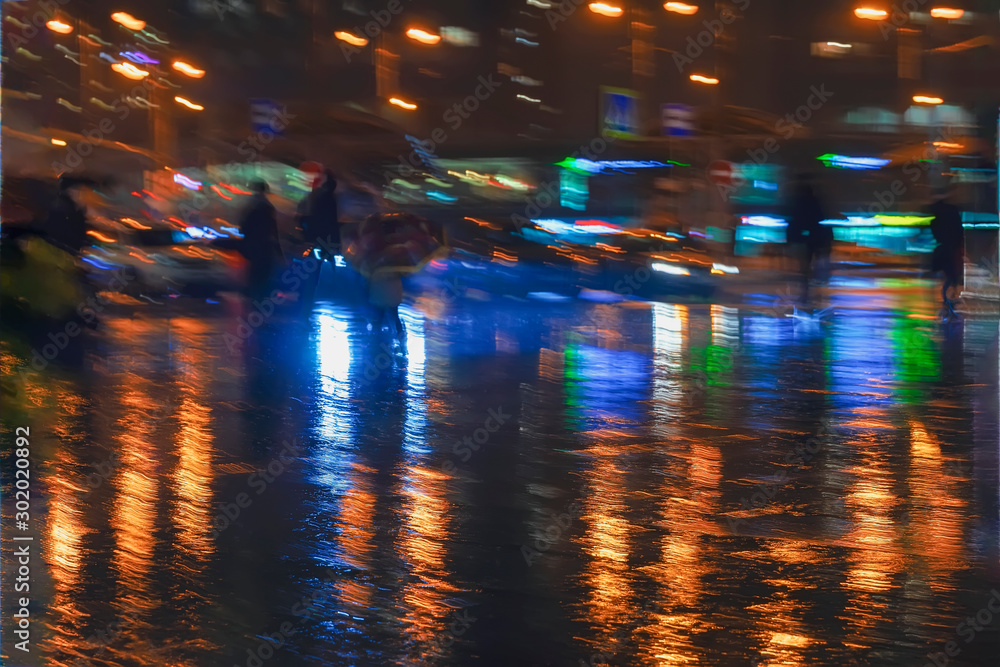 Abstract dark background of modern city at rayny night, bright illumination, reflection on wet asphalt, blurred silhouettes of the walking people