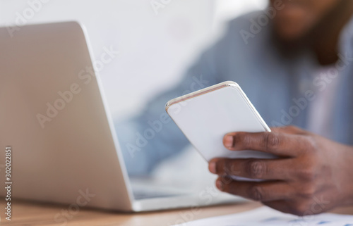 Unrecognizable black entrepreneur using smartphone and working on laptop