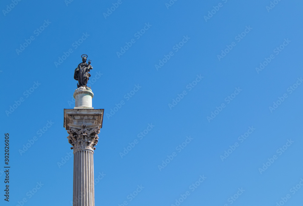 A corinthian  column with Madonna and the child on the top and a blue sky in the background