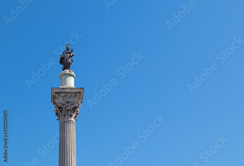 A corinthian  column with Madonna and the child on the top and a blue sky in the background