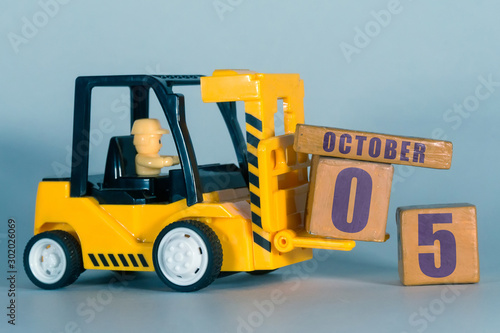 october 5th. Day 5 of month, Construction or warehouse calendar. Yellow toy forklift load wood cubes with date. Work planning and time management. autumn month, day of the year concept