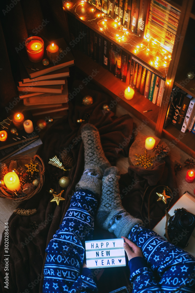  New Year or Christmas atmosphere, girl in blue festive pajamas, warm knitted winter socks with garlands and candles on the background