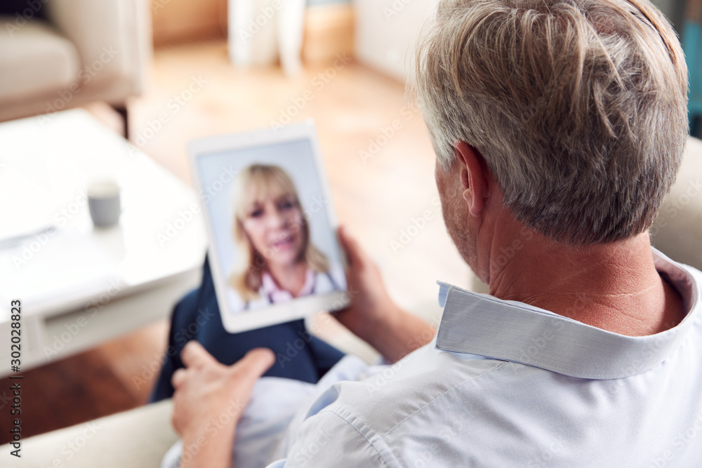 Mature Man Having Online Consultation With Female Doctor At Home On Digital Tablet Mature Man Having Online Consultation With Female Doctor At Home On Digital Tablet