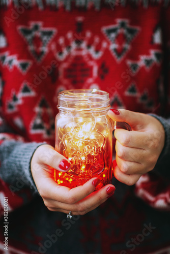 New Year's atmosphere, Christmas, a girl in a red sweater holds a jar with a garland in her hands