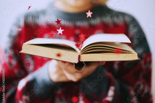  New Year and Christmas, girl blows shiny red stars out of the book in her hands 