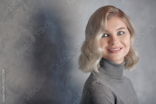 Portrait of a beautiful young woman on a gray background. Happy attractive girl with blonde hair smiles and looks away. Soft lighting. Studio shot of a model. Copy space.