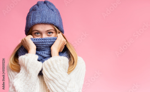 Enigmatic winter girl hiding from cold over pink background