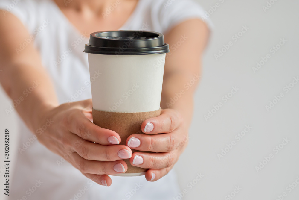 Woman hand holding up a Coffee paper cup isolated on grey background. Front view Woman hand holding up a Coffee paper cup isolated on grey background. Front view
