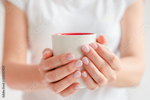 Woman in a white t-shirt holds morning coffee in a white ceramic cup. Christmas concept. Front view