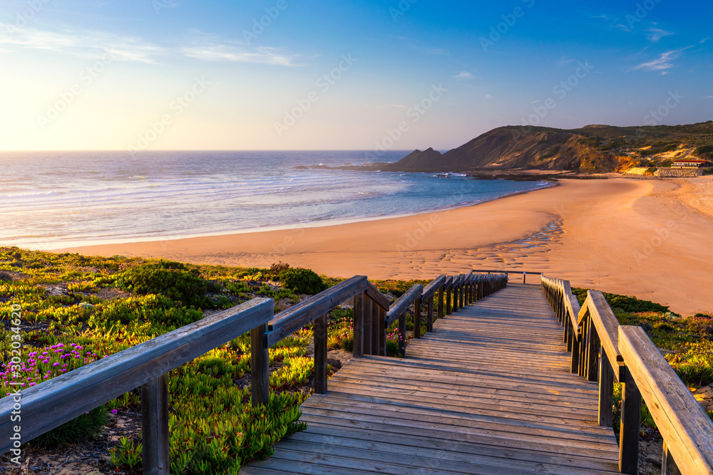 Fototapeta premium Wooden walkway to the beach Praia da Amoreira, District Aljezur, Algarve Portugal. Panorama from Amoreira beach in the Algarve Portugal. Beach and estuary of the Aljezur river, Praia da Amoreira.